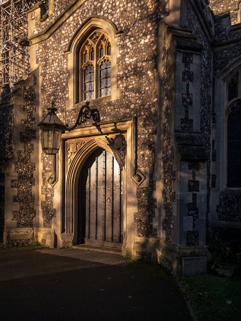 The image depicts the exterior of a historic stone building with a large, arched wooden door set into a decorative stone frame. The building's facade features ornate stonework and tall, narrow windows