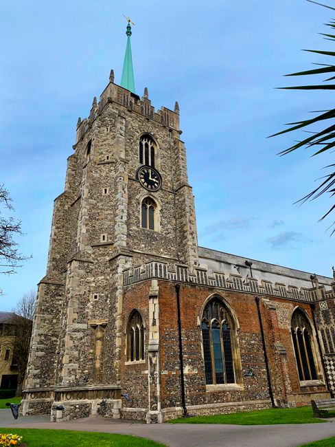 The image depicts the exterior of a historic stone building with a large, arched wooden door set into a decorative stone frame. The building's facade features ornate stonework and tall, narrow windows